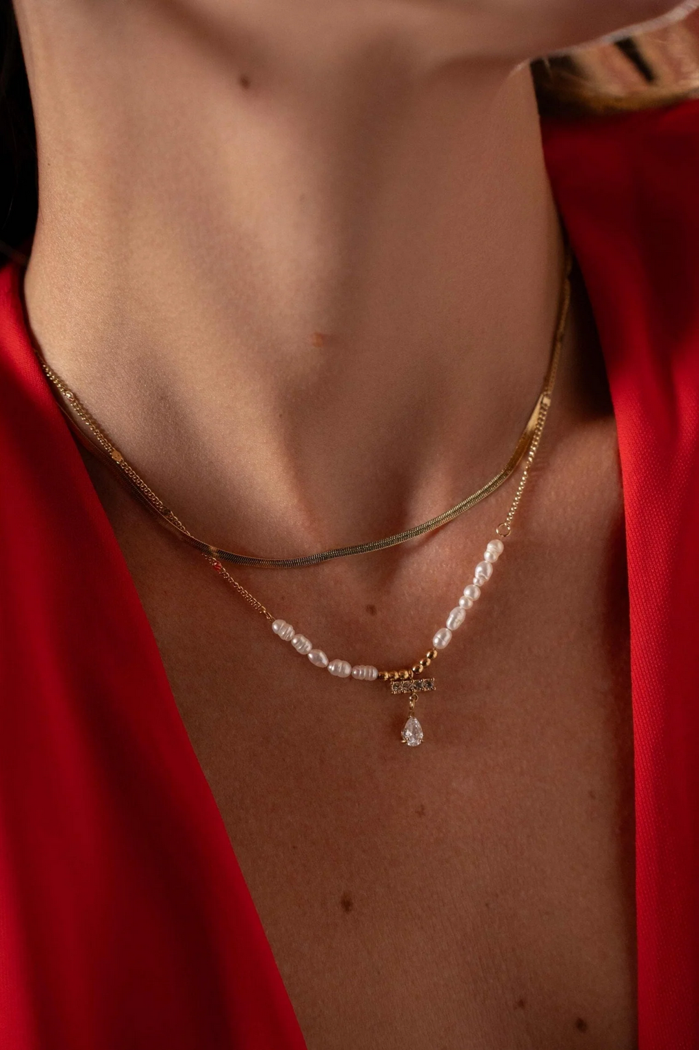 Tyylikäs monikerroksinen kaulakoru helmiyksityiskohdilla ja pisarariipuksella mallin kaulassa.