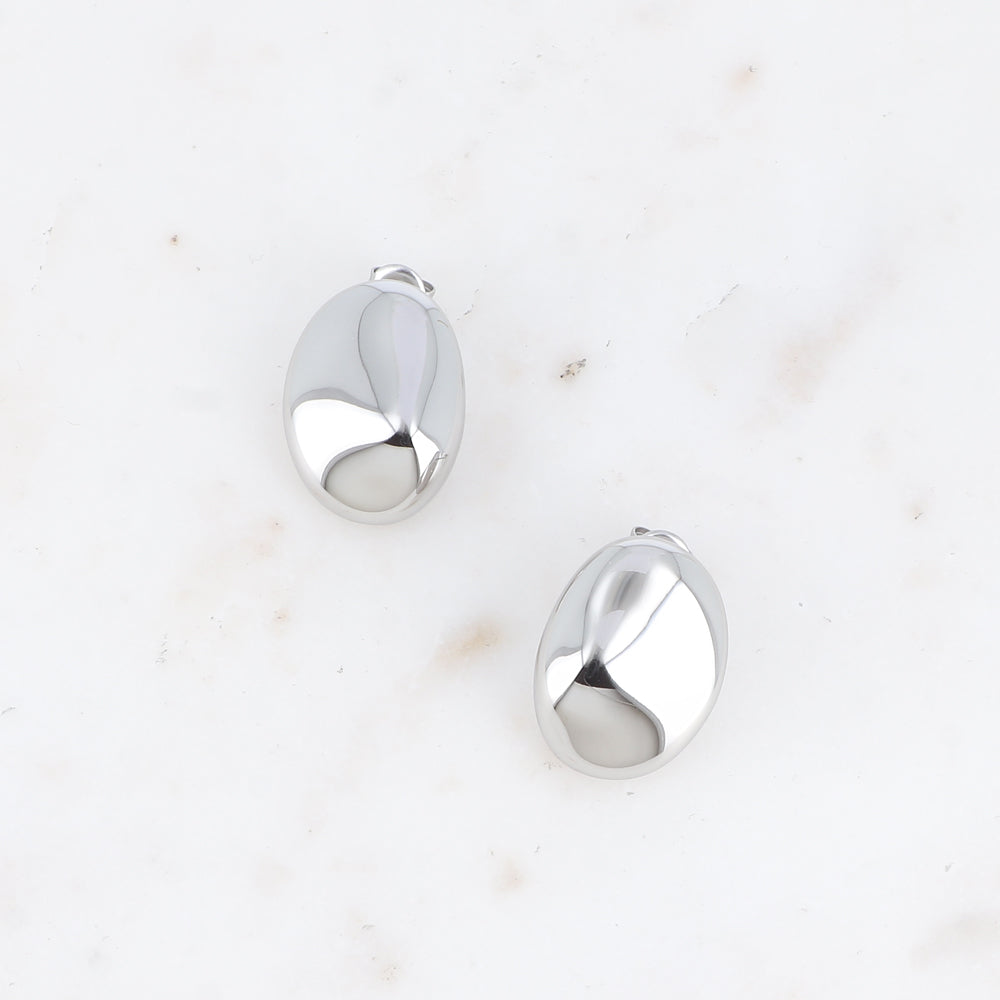 Hopeanväriset suuret ovaalit nappikorvakorut peilipinnalla vaalealla pohjalla.