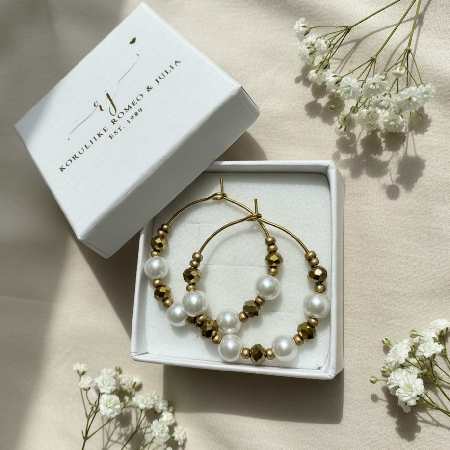 Elegantit Jolie Champagne -korvarenkaat, lähikuva helmien ja kullan sävyisistä yksityiskohdista Romeo & Julia rasiassa.