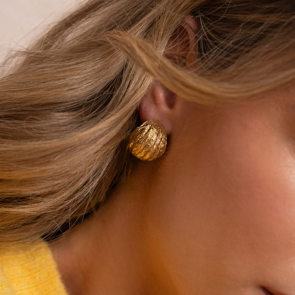 Kullanväriset teksturoidut rengaskorvakorut korvassa lähikuvassa