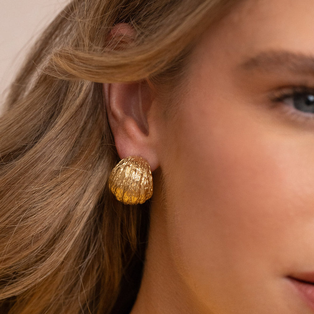 Kullanväriset teksturoidut rengaskorvakorut korvassa lähikuvassa edetäpäin.