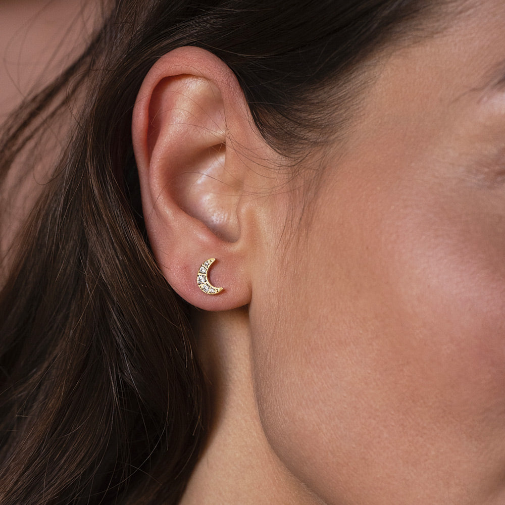 Kullanväriset puolikuun muotoiset korvakorut zirkoniakivillä korvassa.