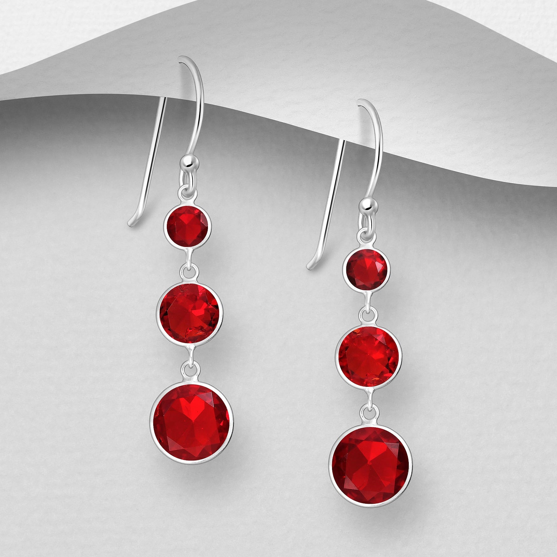 Pitkät roikkuvat hopeakorvakorut punaisilla kristalleilla ja sirolla muotoilulla.