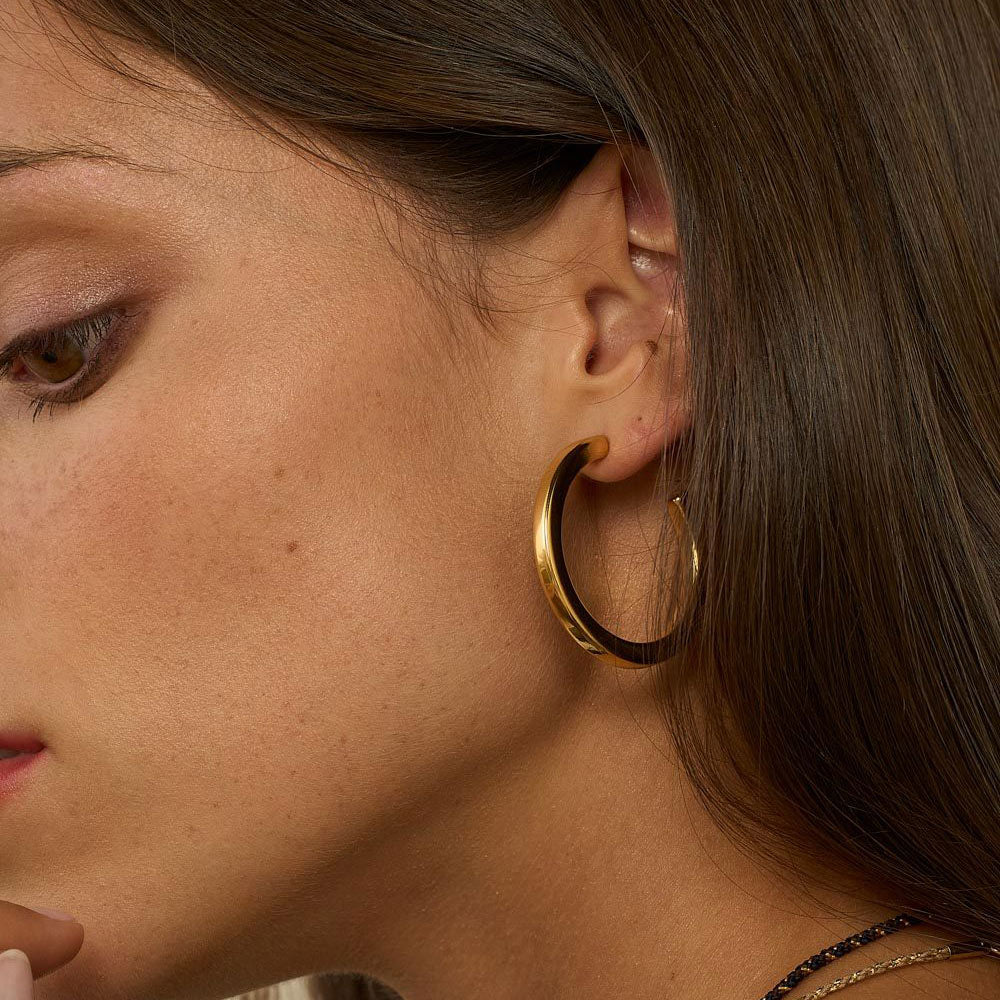 Suuret kullanväriset rengaskorvakorut korvassa lähikuvassa