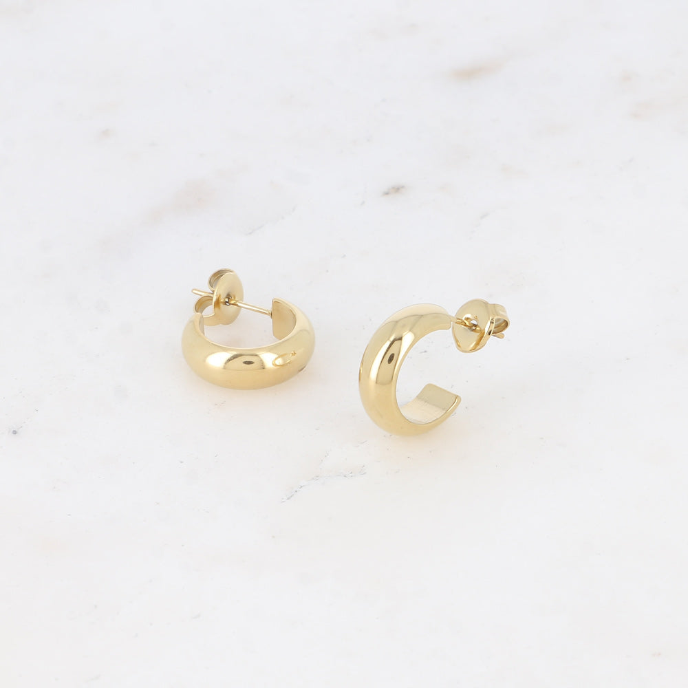 Pienet kullanväriset rengaskorvakorut sileällä pinnalla.