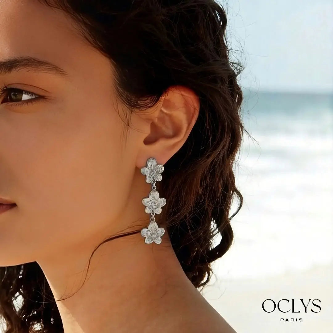 OCLYS Paris Zélie pitkät hopeanväriset klipsikorvakorut mallin korvassa, kolme kauniisti kuvioitua roikkuvaa kukkaa
