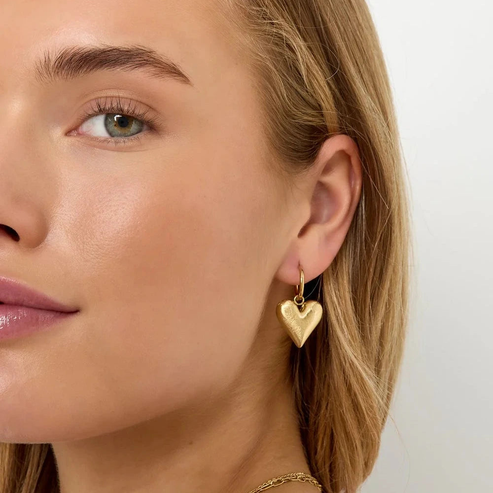 Kultaiset sydänkorvakorut harjatulla pinnalla.