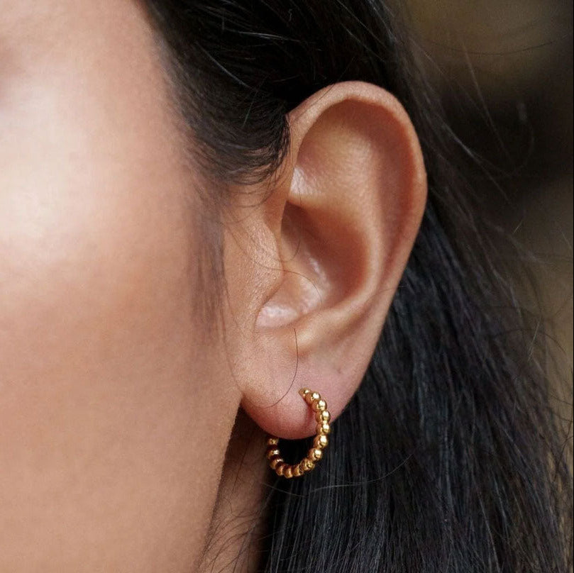 Kullanväriset pienet pallorengaskorvakorut korvassa lähikuvassa