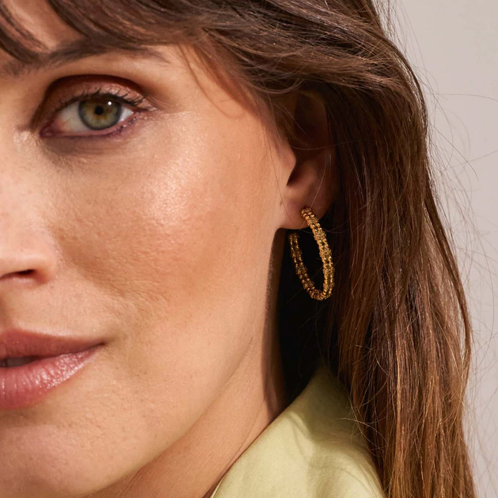 Kullanväriset teksturoidut rengaskorvakorut korvassa lähikuvassa