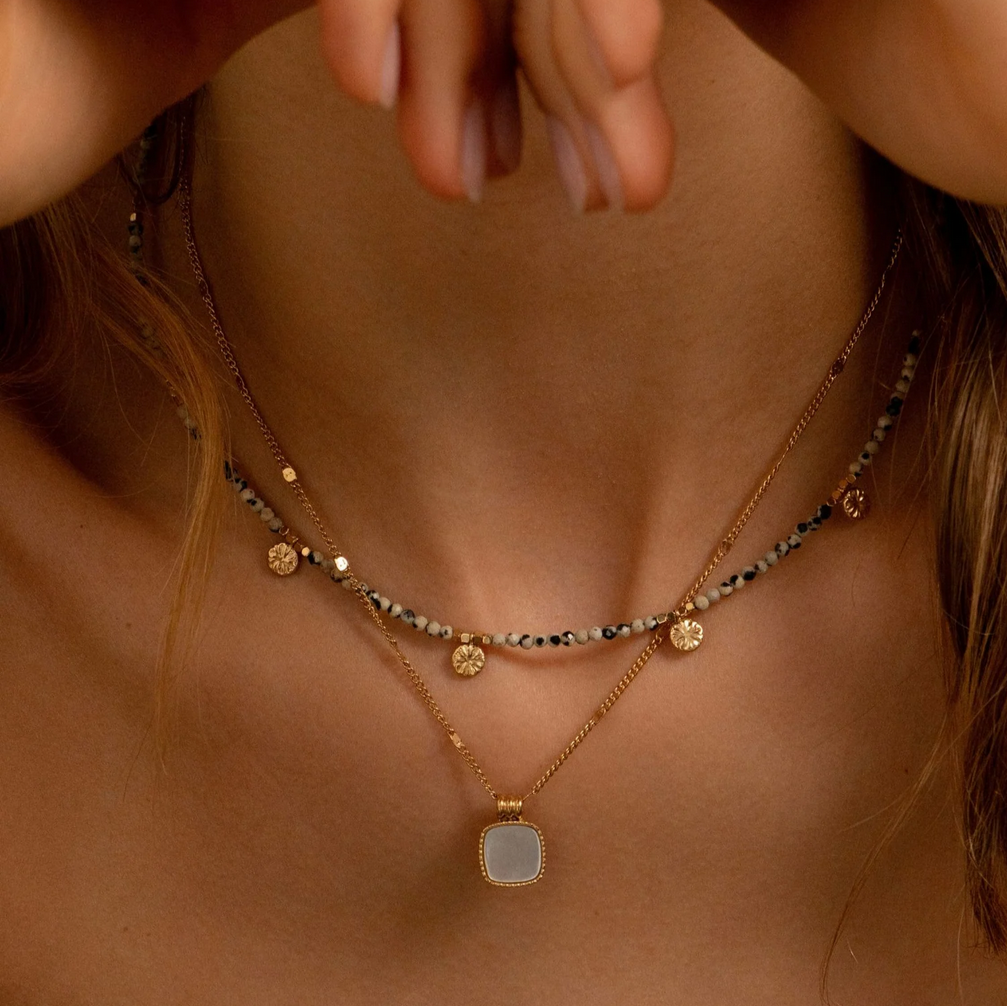 Helmiäisvalkoinen kaulakoru neliön muotoisella riipuksella kaulalla.