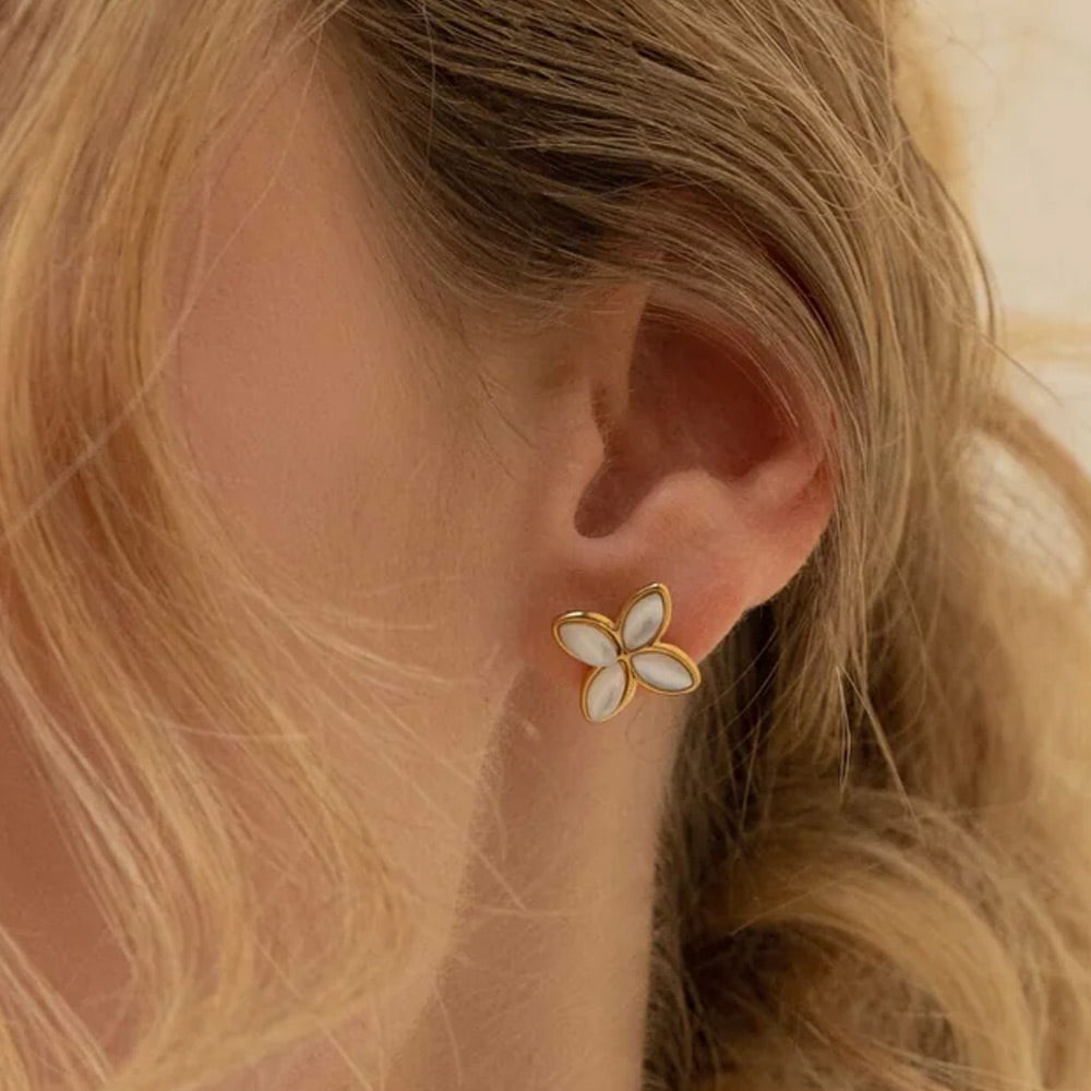 Helmiäisvalkoiset apilanmuotoiset nappikorvakorut kullanvärisellä kehyksellä korvassa.